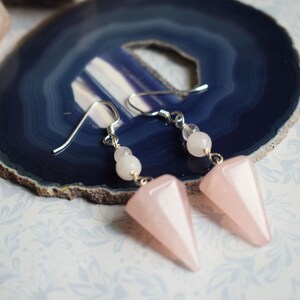 May include: A pair of dangle earrings featuring pink and white gemstone beads and a pink gemstone pendant in the shape of a pyramid.