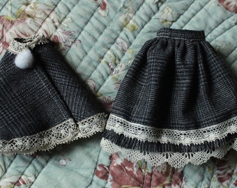 May include: Two grey and white lace trimmed skirts, one a cape style with a white pompom, the other a full skirt.