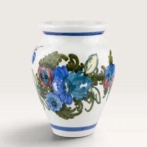 Può includere: Un vaso in ceramica bianca con un motivo floreale dipinto a mano che presenta fiori blu e rossi circondati da foglie verdi. Il vaso ha un corpo largo e arrotondato, un bordo svasato e fasce blu orizzontali che circondano i bordi.