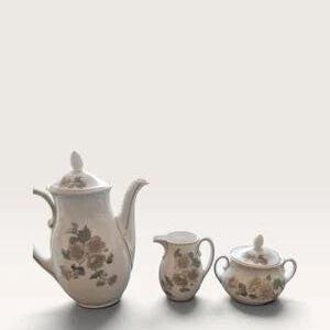 May include: A three-piece porcelain tea set featuring a teapot with a lid, a creamer, and a lidded sugar bowl. Each piece is off-white with a delicate floral pattern in muted brown and green tones, featuring curved handles and elegant spouts.