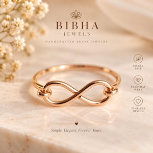 May include: A rose gold-toned infinity symbol ring featuring a smooth, polished metal band. The text BIBHA JEWELS HANDCRAFTED BRASS JEWELRY is displayed above the ring, with the phrase Simple. Elegant. Forever Yours. printed below the jewellery.
