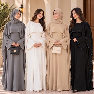 Puede incluir: Cuatro vestidos largos hasta el suelo en gris, blanco, beige y negro. Cada vestido presenta una capa superpuesta con pequeños adornos de cuentas blancas a lo largo de los bordes, mangas largas acampanadas y cuello redondo. Dos vestidos se llevan con hiyabs a juego.