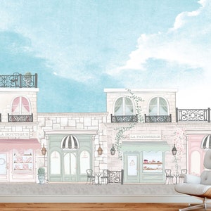 May include: A watercolour illustration of a Parisian street scene with three shops. The shops are labelled "La Boutique", "La Patisserie", and "La Fleurs". The buildings are painted in soft pastel colours with black accents. The sky is a light blue with white clouds.