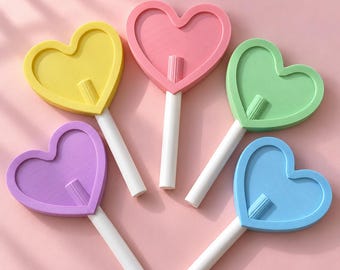 May include: Five heart-shaped lollipop-style objects in yellow, pink, green, purple, and blue. Each heart features a raised border and a central white stick attached to the bottom, creating a uniform design across all five colorful pieces.