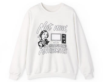 May include: A white long-sleeve crewneck sweatshirt featuring a black graphic print of a person holding a coffee cup next to a computer. The text reads: Not now, I'M CYBERBULLYING ANTISEMITES. The design is in a retro comic book style.