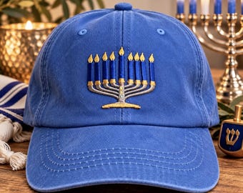 May include: A blue baseball cap featuring an embroidered design of a menorah with nine blue candles and yellow flames. The cap has a structured crown, a curved brim with visible stitching, and a button at the top center of the fabric panels.