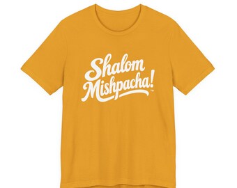 May include: A mustard yellow short-sleeved t-shirt featuring the white text Shalom Mishpacha! printed in a cursive script font across the center of the chest. The garment has a standard crew neckline and a straight hemline.
