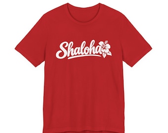May include: A red short-sleeved t-shirt featuring the white text Shaloha in a cursive script font, accompanied by a white hibiscus flower graphic positioned to the right of the lettering on the center of the chest.