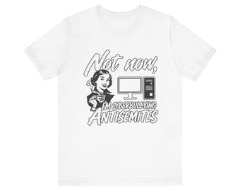 May include: A white short-sleeved t-shirt featuring a black graphic of a person holding a teacup next to a computer. The text reads: Not now, I'M CYBERBULLYING ANTISEMITES. The design is centered on the chest of the garment.