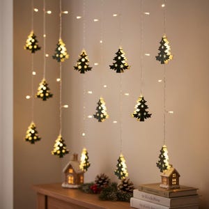 May include: A string of LED curtain lights featuring hanging black cutout Christmas tree ornaments. Each tree shape contains small star-shaped cutouts that allow the warm white light from the internal bulbs to shine through, creating a glowing effect.