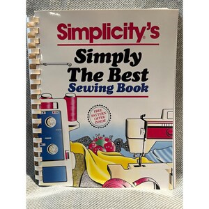 以下が含まれることがあります： スパイラル綴じの裁縫本「Simplicity's Simply The Best Sewing Book」。表紙には、青いロックミシン、白いミシン、赤いピンクッション、黄色い布、ピンクのメジャーのイラストが描かれています。