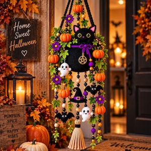 Peut inclure: Une décoration murale d'Halloween composée d'un chat noir crocheté sortant d'une pochette, ornée de citrouilles orange, fleurs violettes, feuilles vertes, fantômes blancs, chauves-souris noires et un chapeau de sorcière, avec un pompon beige.