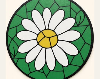 Op de afbeelding: Een ronde onderzetter met een ontwerp in glas-in-loodstijl van een witte margriet met een geel hart. De bloem is geplaatst tegen een groene achtergrond met zwarte lijnen die het patroon verdelen in verschillende geometrische vormen.