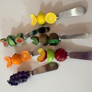 Peut inclure: Un ensemble de quatre couteaux à tartiner en métal avec des manches décoratifs en forme de fruits. Les manches présentent des représentations miniatures de citrons, pastèques, kiwis, oranges, pêches, pommes, prunes et raisins.
