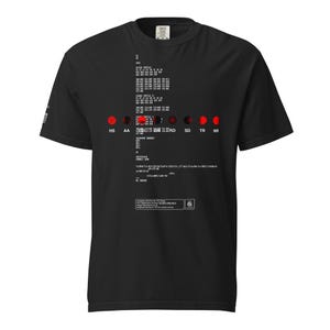 May include: A black short-sleeve t-shirt featuring a white technical data print on the front. The design includes rows of alphanumeric text, a horizontal line of red circular icons, and a rectangular box containing regulatory compliance information.