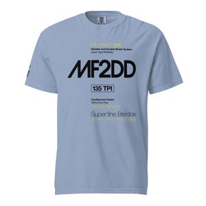 Może przedstawiać: Jasnoniebieski t-shirt z krótkim rękawem z czarnym i żółtym tekstem oraz grafiką. Projekt zawiera tekst MF2DD, 135 TPI, Reliable and Durable Binder System, Super High Reliability, Certified and Tested, 100% Error Free oraz Super fine Beridox.