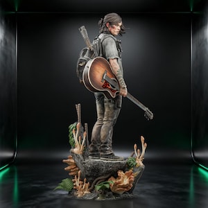 May include: A detailed figurine of a person with shoulder-length dark hair, wearing a grey t-shirt, dark pants, and a backpack, holding a wooden acoustic guitar. The figure stands on a rocky base decorated with various fungi and green ferns.