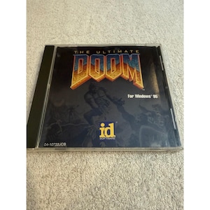Peut inclure: Un boîtier cristal en plastique transparent pour le jeu vidéo The Ultimate Doom pour Windows 95. La pochette présente le titre en grandes lettres jaunes et orange, une illustration sombre d'un personnage et le logo id Software en jaune et blanc.