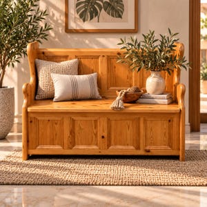 Peut inclure: Un banc de rangement en bois avec un dossier haut et un design à panneaux. Le banc présente une finition brun clair et est agrémenté d'un coussin carré texturé, d'un coussin rectangulaire à rayures grises, d'un bol en bois et d'un vase en céramique.