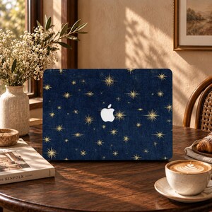May include: A dark blue laptop skin featuring a repeating pattern of gold starbursts and sparkles. The design includes a central cutout for the Apple logo, showcasing a deep navy background with a textured appearance and various sized stars.
