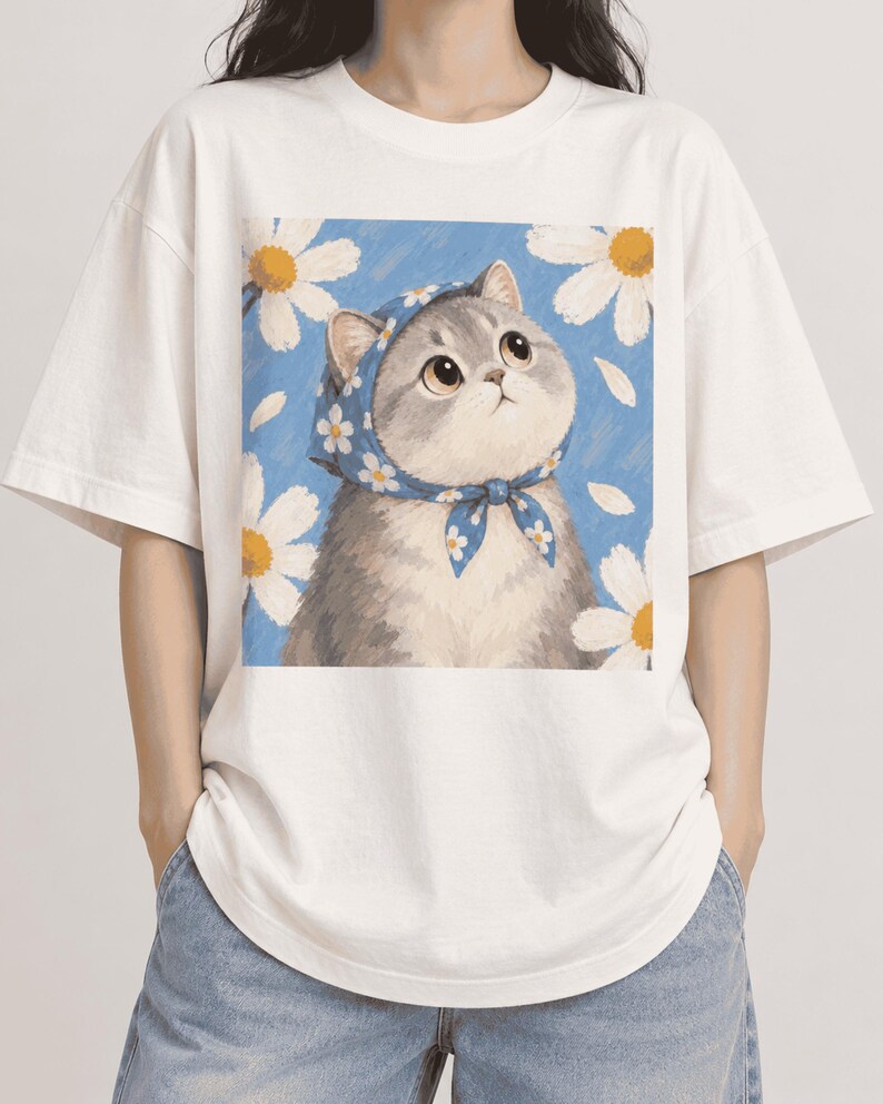 Model wearing a cream oversized T-shirt printed with a gray cat in a blue scarf surrounded by white daisies.