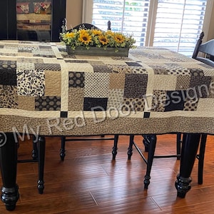 Op de afbeelding: Een rechthoekige quilt met een patchworkontwerp van diverse vierkante en rechthoekige stoffen blokken in tinten zwart, cr&egrave;me en beige. De quilt toont diverse patronen, waaronder bloemmotieven, geometrische vormen en paisley-prints met een rand.