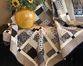 May include: A patchwork quilt featuring a variety of brown, tan, and cream fabric squares with diverse floral, geometric, and paisley patterns. The quilt is draped over a surface, showcasing intricate machine quilting stitches throughout the fabric.