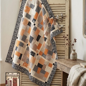 Könnte beinhalten: Ein Patchwork-Quilt mit einem Raster aus Quadraten in Orange-, Schwarz-, Weiß- und Grautönen mit verschiedenen Blumen- und geometrischen Mustern. Der Quilt hat einen breiten schwarzen Rand mit weißem Blumenmuster und liegt über einem Holzladen.