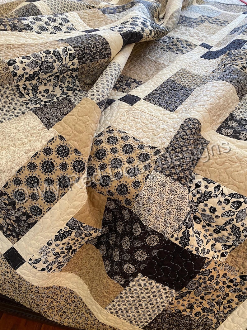 Op de afbeelding: Een patchwork quilt bestaande uit diverse vierkante stoffen blokken in tinten zwart, wit en beige. De quilt toont uiteenlopende patronen zoals bloemmotieven, geometrische vormen en bladeren, met zichtbare machinale stiknaden over het geheel.