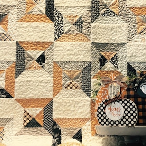 Puede incluir: Un fondo de tela acolchada con un patr&oacute;n geom&eacute;trico en crema, naranja y negro. En primer plano, se muestran dos decoraciones de madera con forma de calabaza. Una presenta lunares blancos y negros con el texto "hocus pocus".