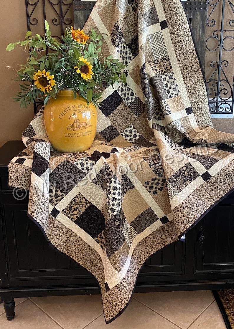 Op de afbeelding: Een patchwork quilt met een verscheidenheid aan bruine, beige en cr&egrave;mekleurige stoffen vierkanten met diverse bloem-, geometrische en paisley-patronen. De quilt is over een oppervlak gedrapeerd en toont ingewikkelde stikselpatronen.