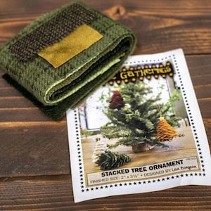 Puede incluir: Un kit para hacer un adorno de árbol apilado, con un primer plano de las piezas de tela y una foto del adorno terminado. El adorno mide 5 cm por 9 cm y está diseñado por Lisa Bongean.