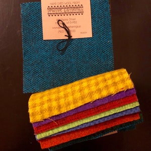 Può includere: Un mucchio di tessuto di lana tinto a mano in vari colori, tra cui giallo, rosso, viola, verde e blu. Il tessuto è disposto a forma di arcobaleno. Un biglietto da visita per Primitive Gatherings è visibile nell'angolo in alto a sinistra dell'immagine. Il biglietto include il nome dell'azienda, l'indirizzo, il sito web e il numero di telefono.