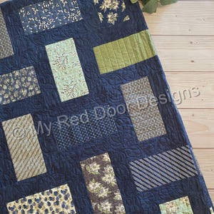 Könnte beinhalten: Eine Patchwork-Decke mit dunkelblauem Hintergrund und einem geschwungenen Steppmuster. Die Decke besteht aus verschiedenen rechteckigen Stoffblöcken in Grün-, Weiß- und Blautönen, die florale, gestreifte und gepunktete Muster aufweisen.