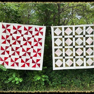 May include: Two handmade quilts hanging on a clothesline outdoors. The quilt on the left is red and white with a pinwheel pattern. The quilt on the right is green, white, and pink with a diamond pattern.