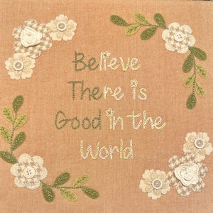May include: Beige fabric with embroidered green vines and white flowers. The text "Believe there is good in the world" is embroidered in the center.