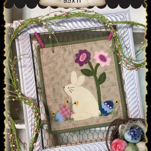 Könnte beinhalten: Ein gerahmter, gesteppter Wandbehang mit einem weißen Hasen, Blumen und Ostereiern. Der Titel "Bunny Love 9.5x11" befindet sich auf dem Rahmen.