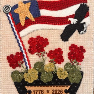 May include: A rectangular fabric wall hanging featuring a black planter with red geraniums, a waving American flag with a gold star, and a soaring bald eagle. A tan wooden plaque attached to the planter is engraved with the text 1776 star 2026.