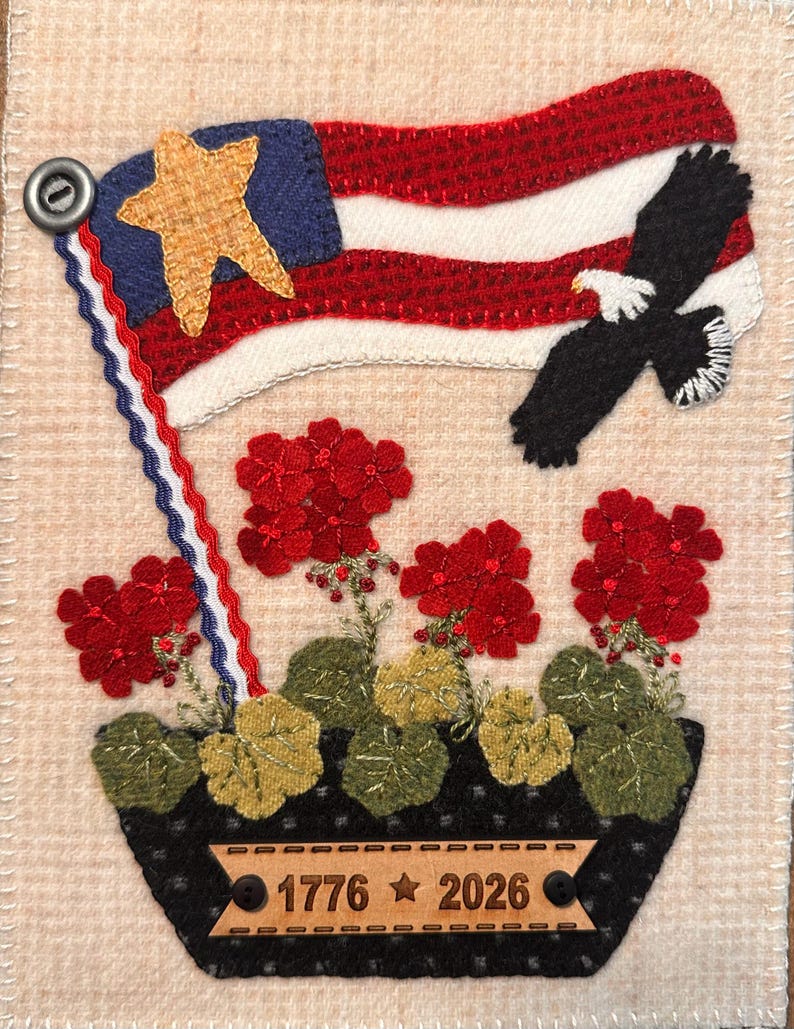 May include: A rectangular fabric wall hanging featuring a black planter with red geraniums, a waving American flag with a gold star, and a soaring bald eagle. A tan wooden plaque attached to the planter is engraved with the text 1776 star 2026.