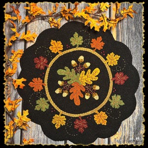 Może przedstawiać: Czarna podkładka z falistymi krawędziami z haftowanym wzorem jesiennych liści i żołędzi. Centralnym motywem jest okrągły układ kolorowych liści i żołędzi, otoczony złotą obwódką. Ozdobne jesienne liście ułożone wokół podkładki.