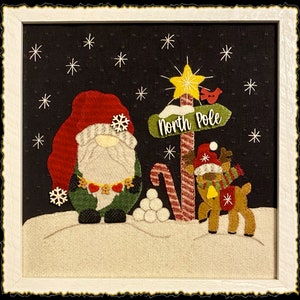 May include: A felt Christmas scene with a gnome, a reindeer, and a sign that reads "North Pole". The scene is set against a black background with white snowflakes.
