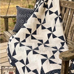 May include: A navy blue and white quilt featuring a repeating pinwheel block pattern with small floral and geometric prints. The quilt is draped over a wooden bench alongside a matching navy blue and white throw pillow with a small floral pattern.
