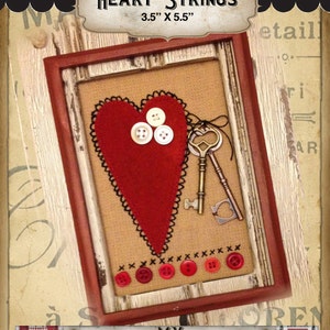 Può includere: Un ricamo a punto croce incorniciato che presenta un cuore di feltro rosso con bottoni e chiavi. La cornice è in legno con una finitura usurata. Il titolo "HEART STRINGS" e la dimensione "3.5" x 5.5" sono scritti sulla cornice. La parte inferiore dell'immagine presenta il testo "MY RED DOOR DESIGNS".