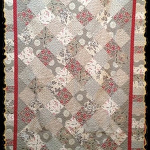 May include: A rectangular quilt featuring a diamond-patterned center composed of various fabric squares in shades of gray, beige, and red with floral and polka dot prints. The quilt is framed by a solid red border and a decorative scalloped edge.