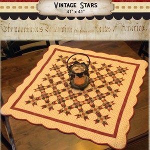 May include: A square fabric table topper titled Vintage Stars measuring 41 inches by 41 inches. The quilt features a cream background with a repeating pattern of dark red and navy blue stars, finished with a scalloped edge and a dark red border.