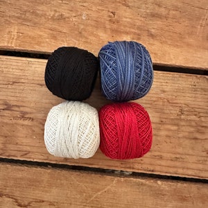 May include: Four balls of yarn in different colors: black, white, blue, and red. The yarn is wound into balls and is ready for knitting or crocheting.