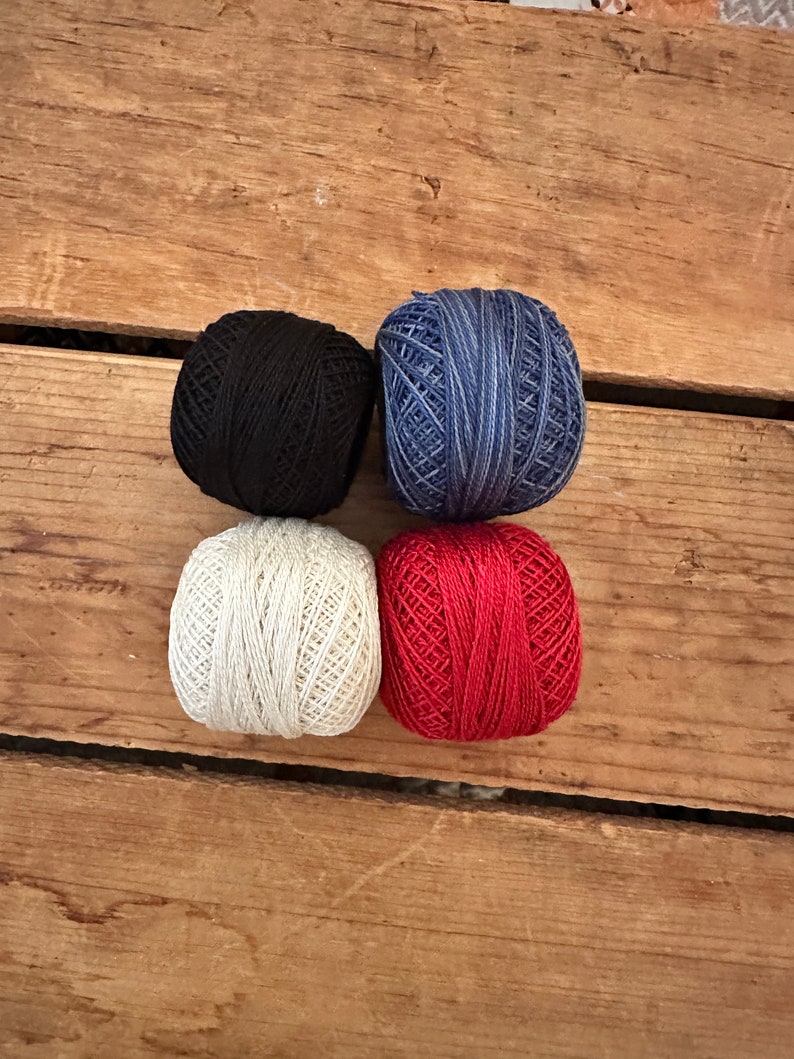 May include: Four balls of yarn in different colors: black, white, blue, and red. The yarn is wound into balls and is ready for knitting or crocheting.