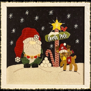 May include: A felt Christmas scene featuring a gnome, a reindeer, and a sign reading "North Pole". The scene is set against a black background with white snowflakes.