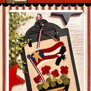 May include: A patriotic wall hanging with a flag and eagle design. The artwork features a flag with a gold star, red and white stripes, and a black eagle. The dimensions are approximately 6.5 inches by 8.5 inches.