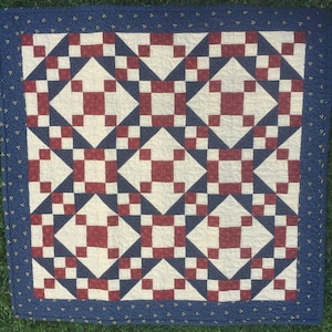 May include: A red, white, and blue quilt with a geometric pattern. The quilt is made of squares and triangles and has a blue border.